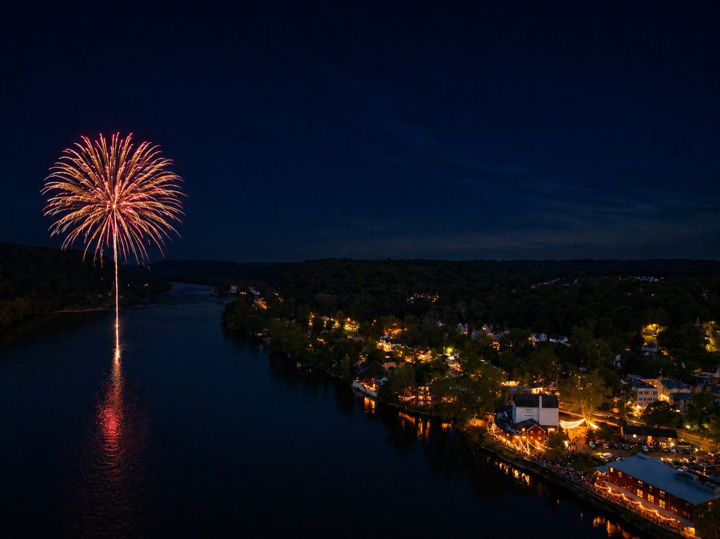 Aerial view of a single firework over the Delaware River, New Hope glowing along the shore